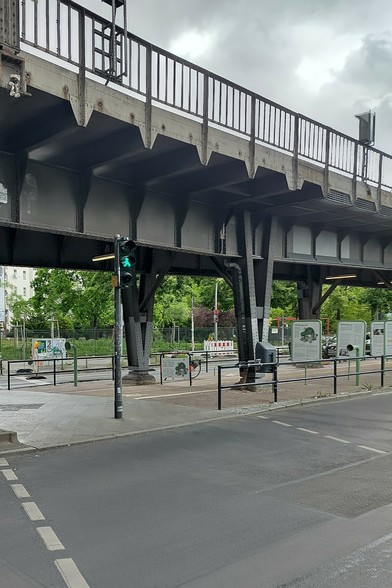 Foto einer Fußgänger*innenfurt mit Ampel, die gerade grün zeigt. Darüber die Hochbahn Skalitzer Straße. Unter der Hochbahn ist rechts entlang der eingerichtete 200m Fahrradweg / die Erlebnisstrecke zu sehen. 